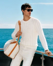 Model wearing sunglasses and white sweater holding a duffel bag on a boat deck