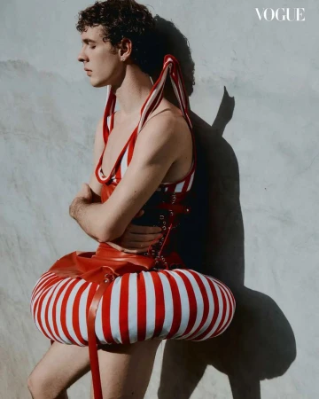 Fashion editorial shot of a male model in avant-garde striped red and white outfit, posing against a neutral background, with 'Vogue' logo visible.