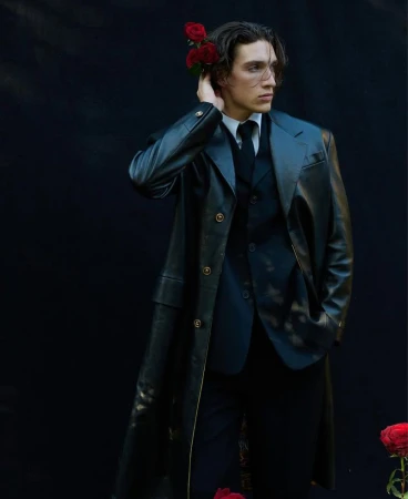 A stylish, young adult male model wearing a black leather coat, vest, and trousers, complemented by red roses against a dark backdrop.