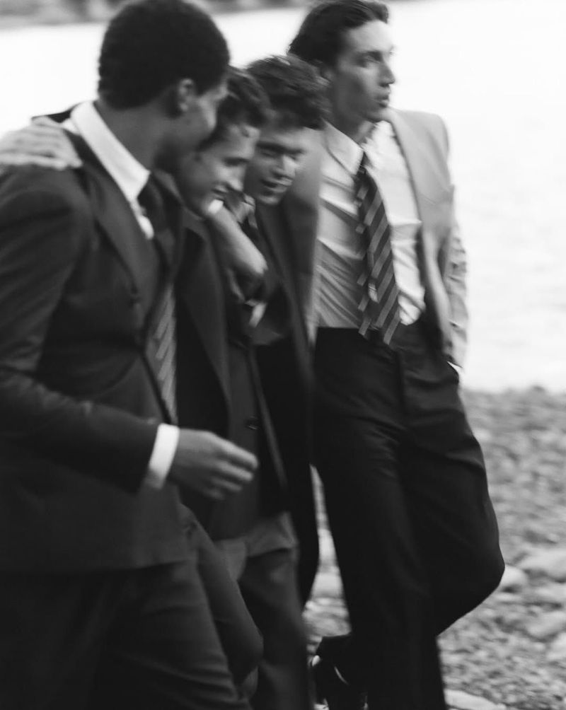 Black and white photo of four men in suits standing near a body of water, looking off into the distance, wearing formal attire.