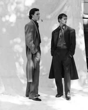 Two male models in tailored coats standing in profile against a light backdrop for M Le magazine du Monde