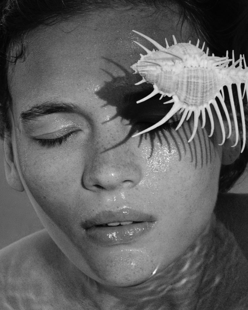 Monochrome portrait of a woman with a closed eye and a shell on her forehead, creating a shadow on her face, wet skin and hair.