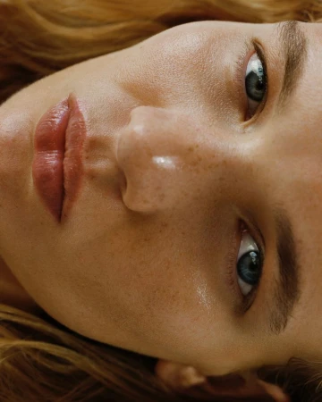 Close-up portrait of model Caitlin Soetendal showing dewy freckled skin, blue eyes, and natural pink lips for AnOther Magazine.
