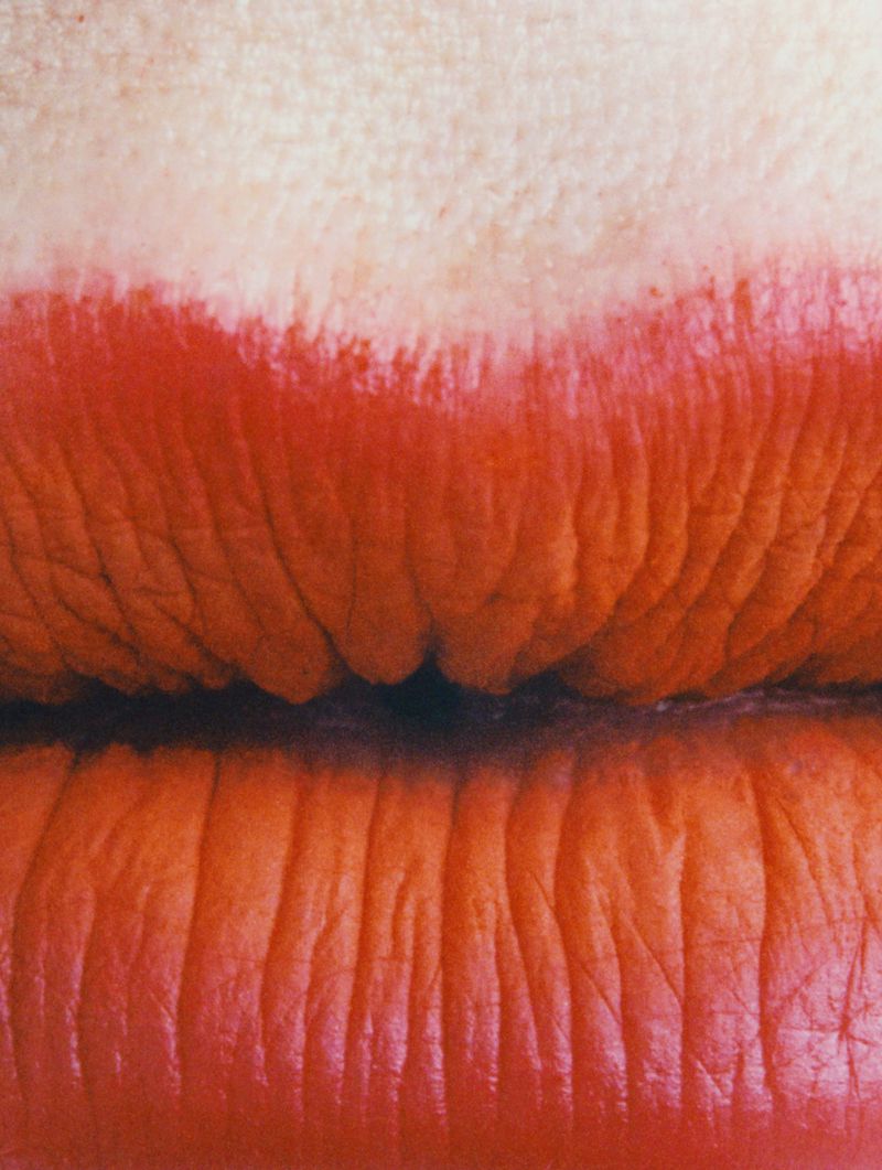 Macro shot of red lipstick on human lips, emphasizing texture and color. Close-up shot showcasing the details of makeup application.