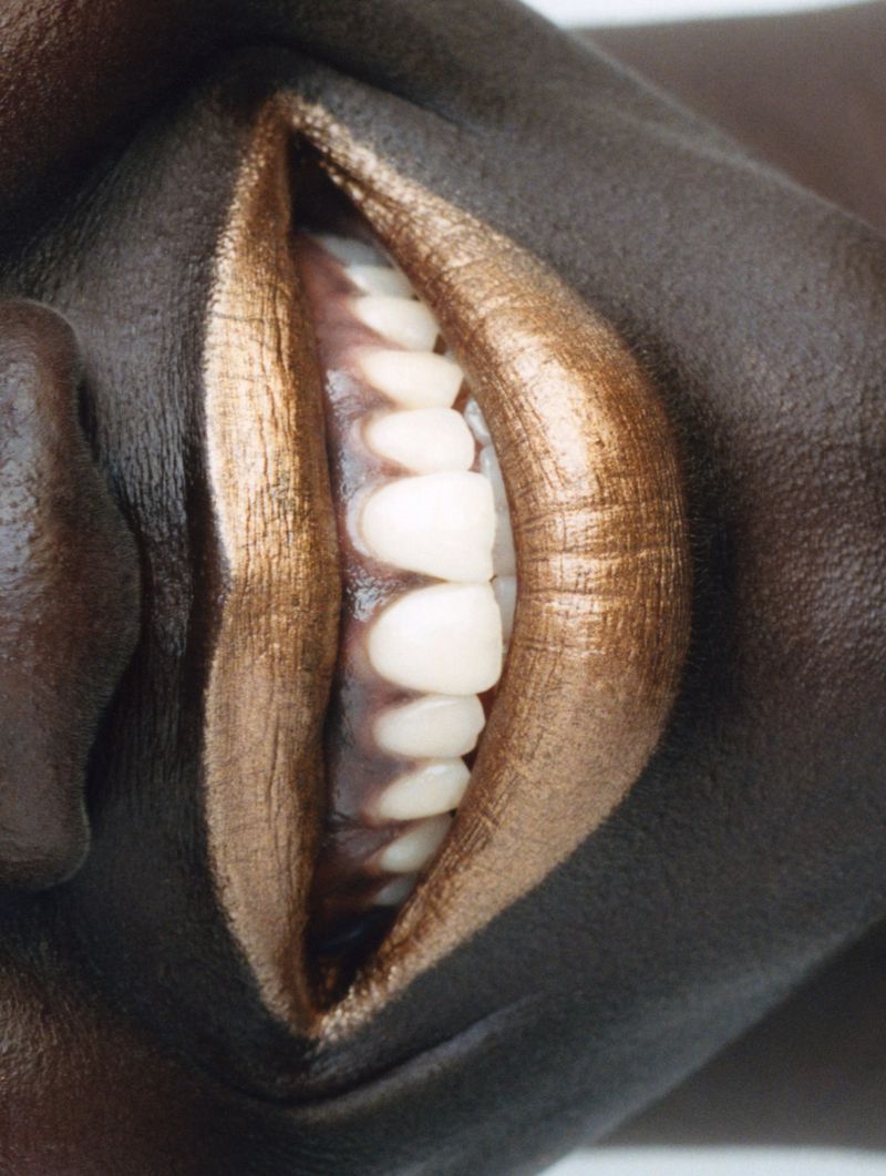 Close-up studio shot of a dark-skinned woman with gold lipstick, showcasing teeth. Focus on beauty and cosmetics concept.