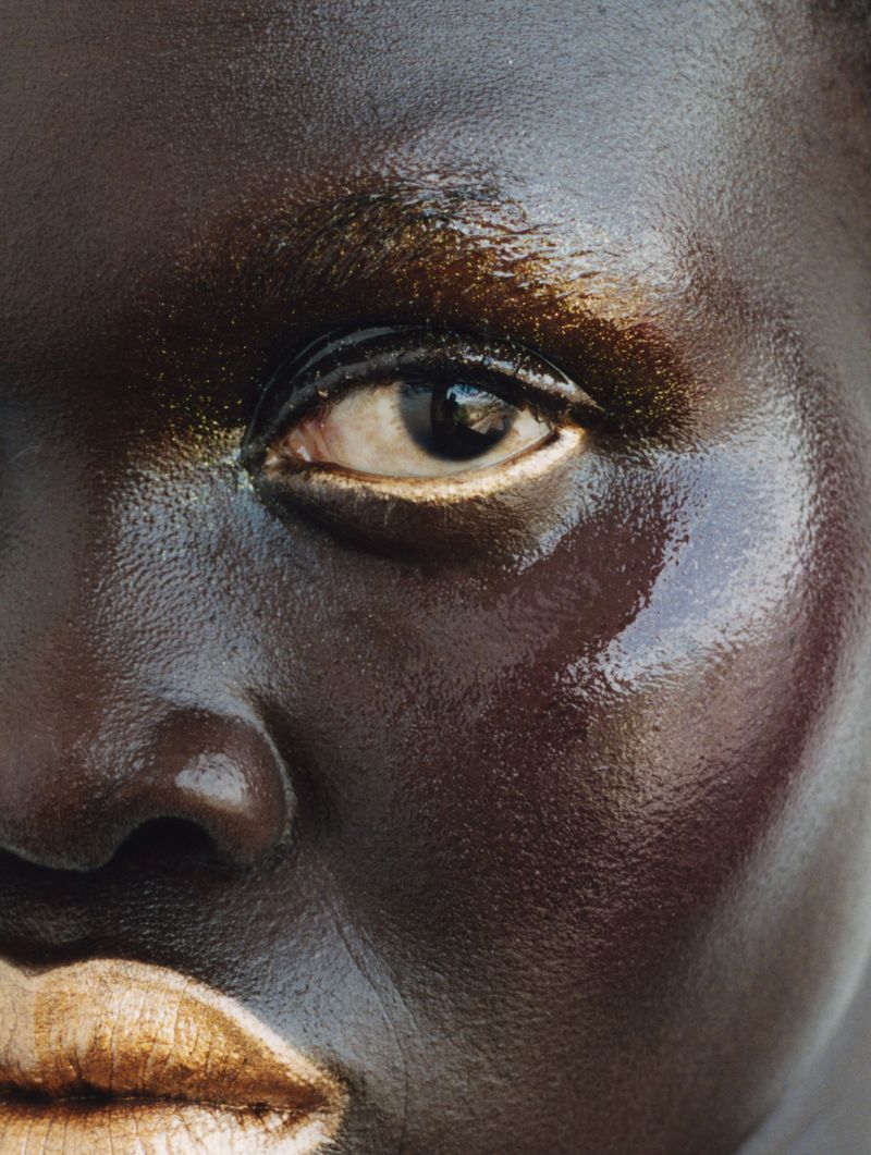 Close-up portrait of an adult female of African descent with bronze and golden-hued makeup, showcasing detailed beauty and cosmetic artistry.