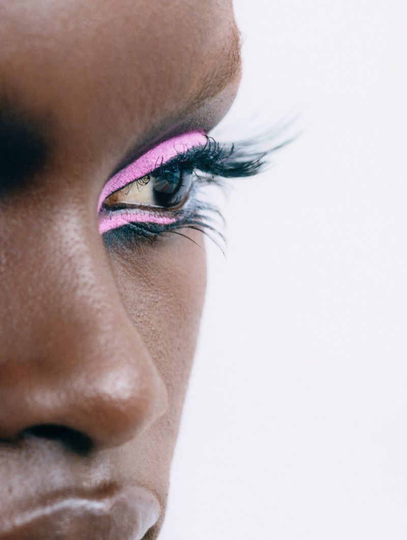 Extreme close-up of an African American woman's eye with pink eyeshadow and dramatic black lashes on a white background.