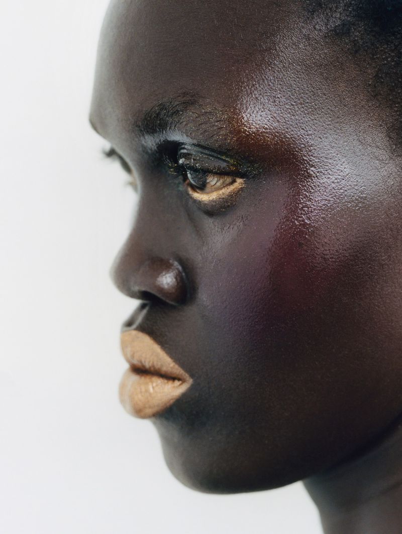 Close-up of an adult female with dark skin and beige lipstick, in profile against a bright background, focusing on beauty and skincare.