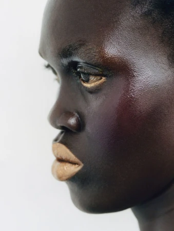 Close-up of an adult female with dark skin and beige lipstick, in profile against a bright background, focusing on beauty and skincare.