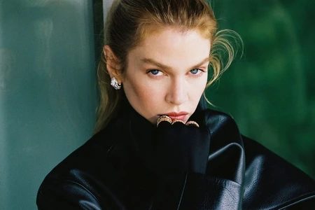 Model Stella Maxwell wearing a black leather jacket and black turtleneck with rings near her lips in a close-up portrait.