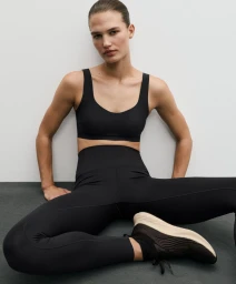 Model Emmi Freeman sits on the floor wearing a black sports bra and matching high-waisted leggings for Oysho's Training Season.