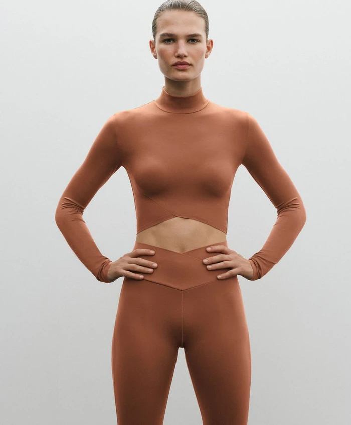 Model wearing a brown activewear set with a long-sleeve crop top and leggings against a seamless grey background