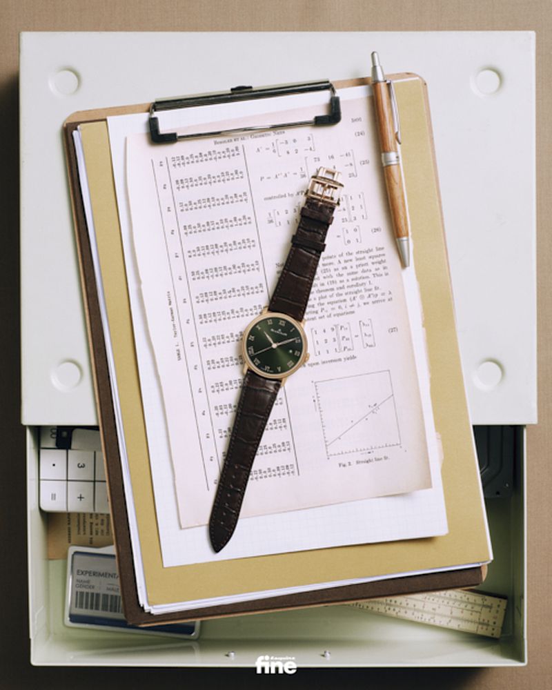 Elevated view of a brown leather wristwatch, wooden pen, and clipboard with diagrams atop an open filing cabinet drawer.