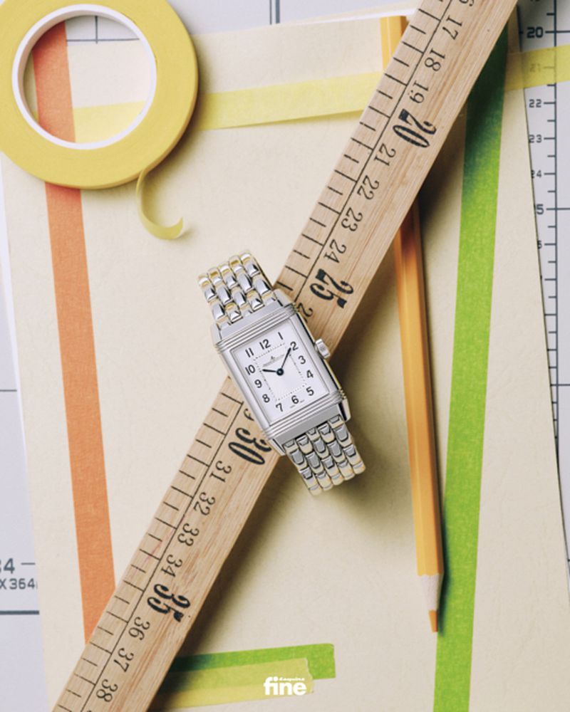 Elevated shot of a silver wristwatch balanced on a wooden ruler with colored tape, pencil, and paper creating a visually engaging flat lay.