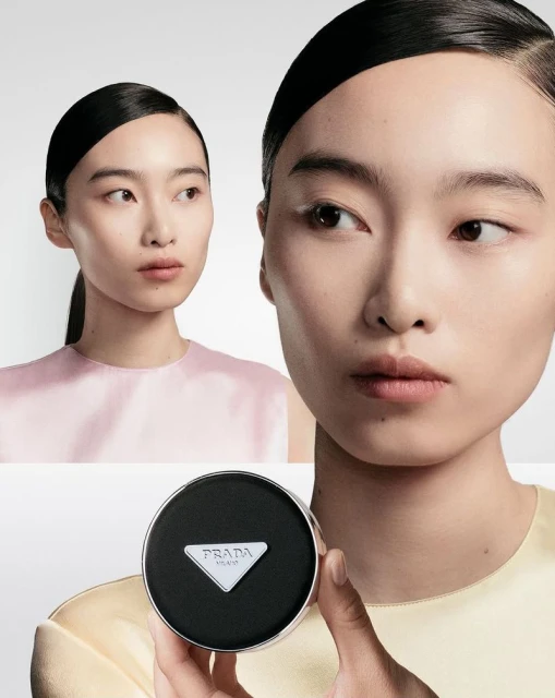 Asian woman poses in a beauty shot featuring Prada makeup. She holds the compact product in her hand near her face.