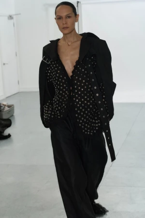 A fashion photo showcasing an adult woman in a black outfit with silver grommets, posing in a bright white studio setting.