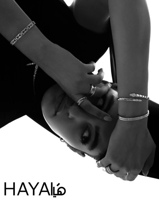 Close-up black and white shot featuring a model adorned with multiple bracelets and rings, showcased against a stark, light background.