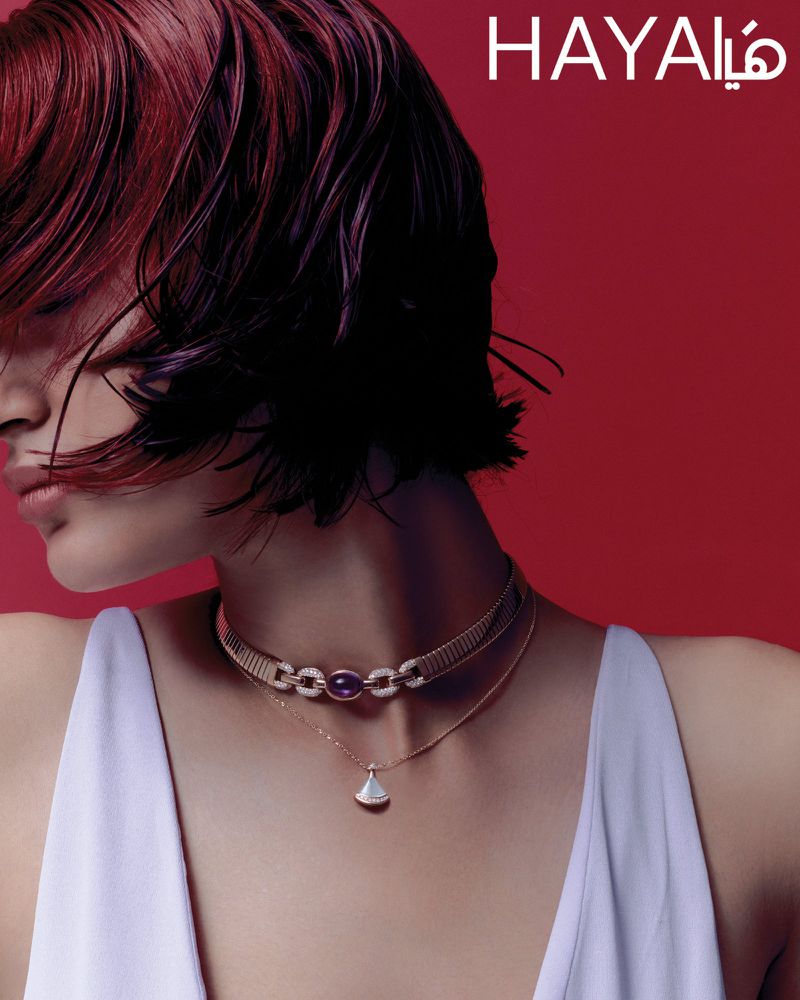 Close-up of an adult woman with burgundy hair wearing jewelry in front of a red background. Beauty shot for fashion and style.