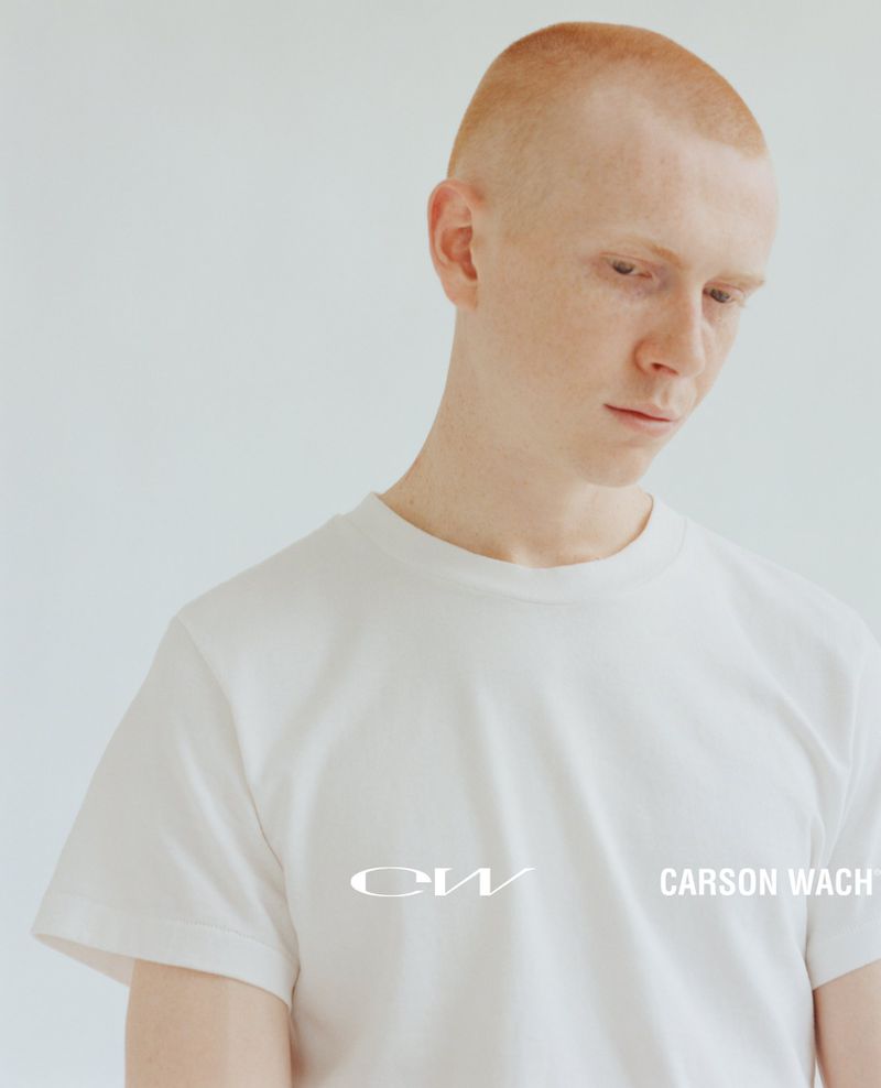 Portrait of a young adult male with very short, reddish hair. He is wearing a white t-shirt. The background is plain and white.