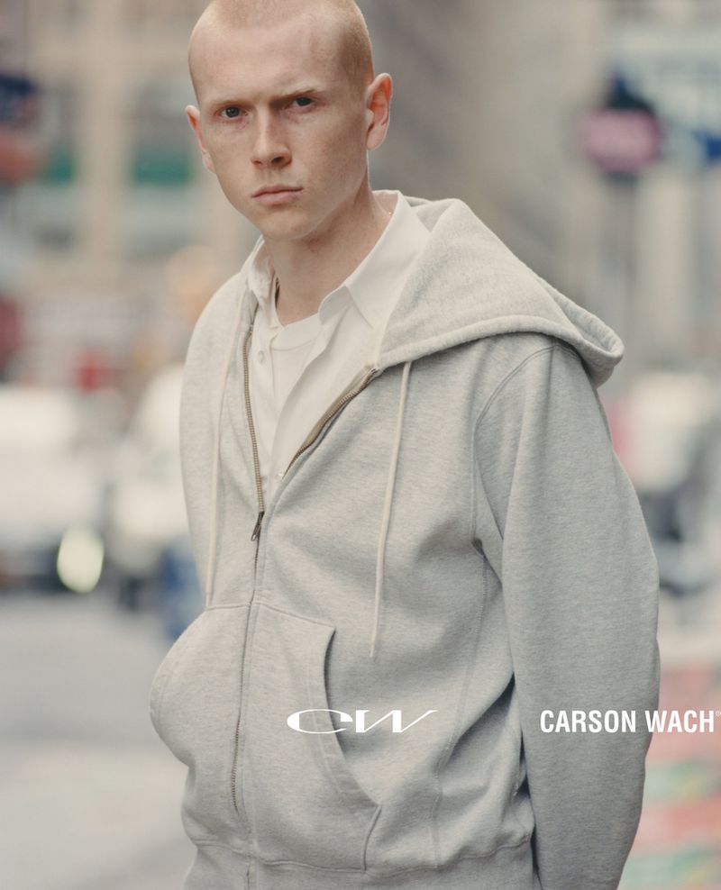 Man in grey zip-up hoodie standing on city street. White collared shirt visible underneath. 'CW CARSON WACH' text on hoodie.