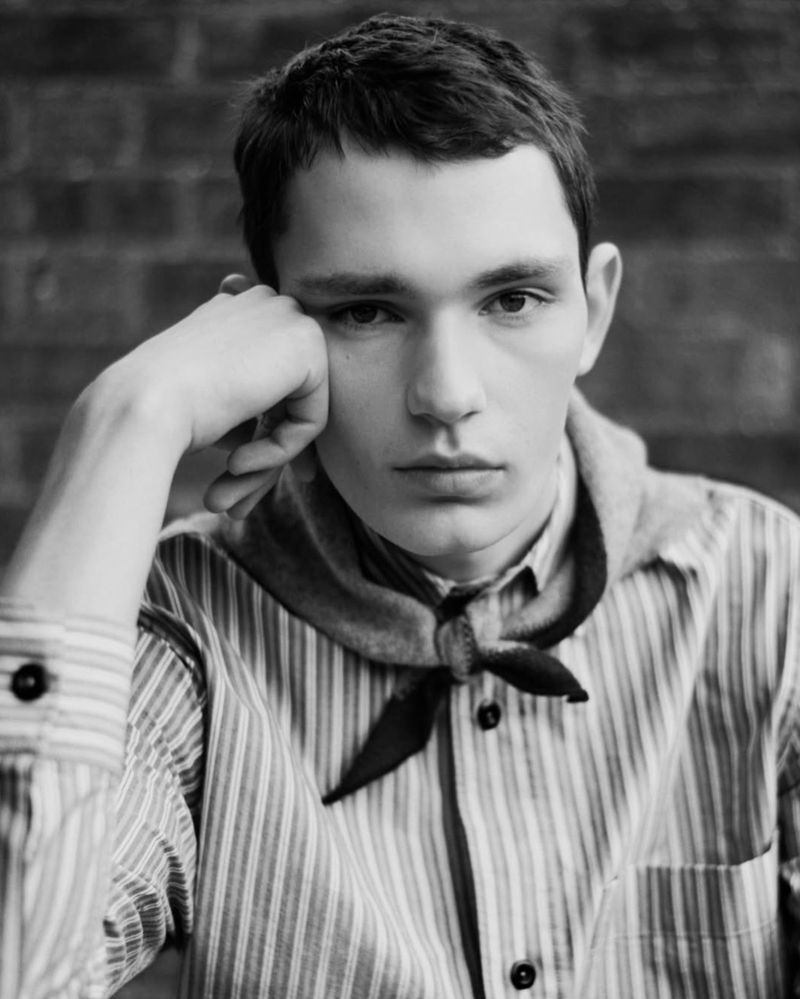 Portrait of a young man with fair skin and short dark hair, resting his head on his hand, wearing a striped shirt and bandana.