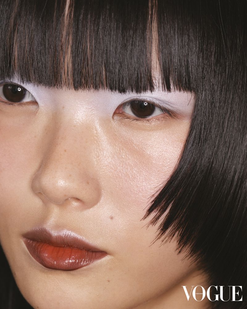Close-up portrait of a woman with a black bob hairstyle, white eye makeup, and glossy red lipstick, with the VOGUE logo visible.