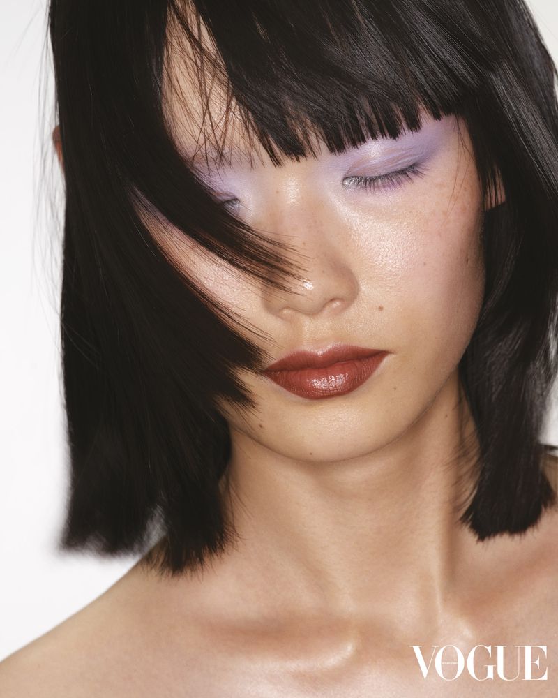 Headshot of a dark-haired woman with fair skin and light purple eyeshadow posing in front of a white background with soft lighting.