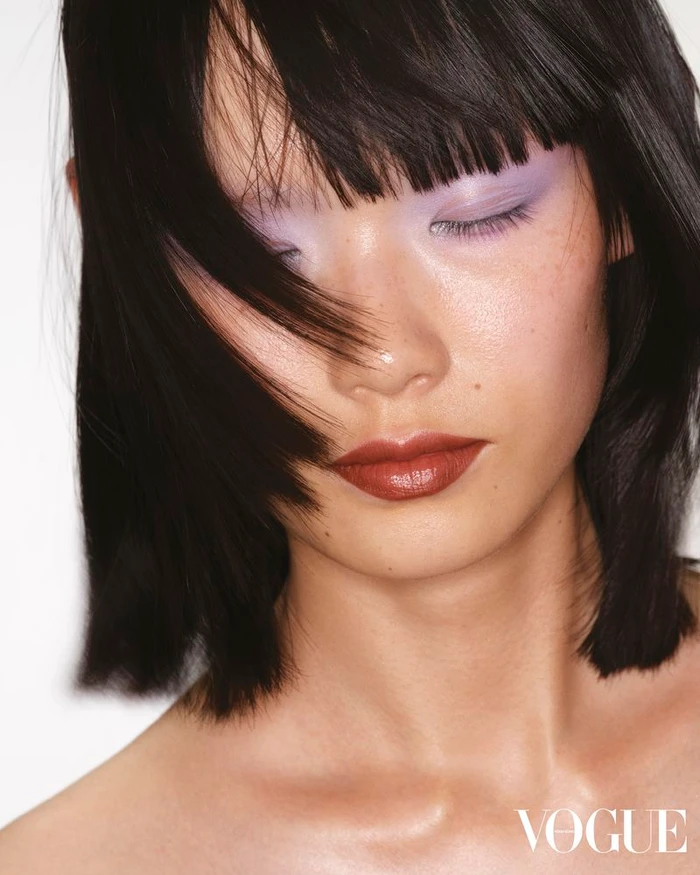 Close-up portrait of model Xie Chaoyu with lavender eyeshadow and dark hair falling across her face for Vogue Hong Kong.