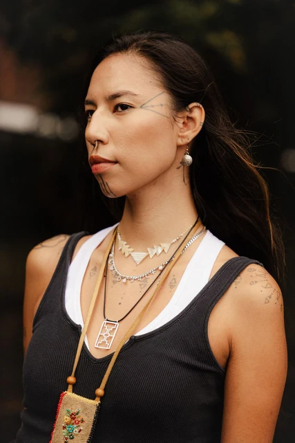 Portrait of an Indigenous woman with traditional face tattoos wearing multiple necklaces outdoors, focusing on fashion and cultural representation.