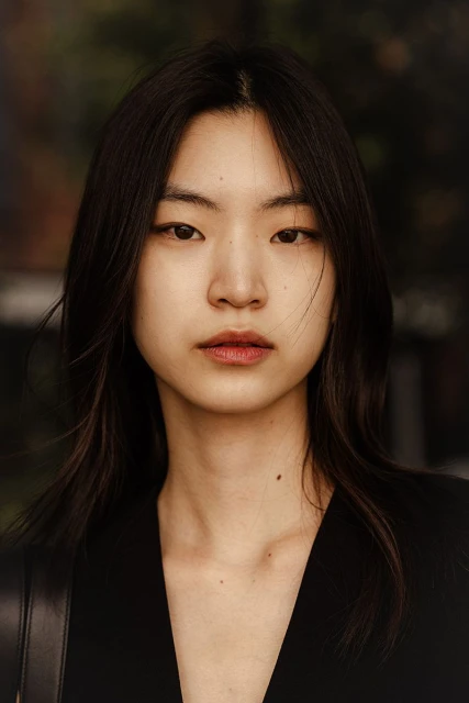 Close-up portrait of an Asian woman with long dark hair wearing a black top, shot in natural light with a blurred background.