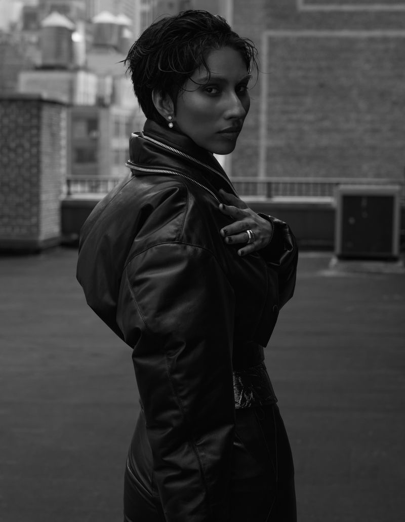 Black and white portrait of an adult female with dark short hair and leather jacket in a rooftop environment overlooking a city.