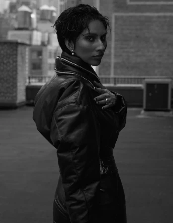 Black and white portrait of an adult female with dark short hair and leather jacket in a rooftop environment overlooking a city.