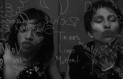 Black and white editorial portrait of two models gazing through glass inscribed with handwritten text for Vogue Netherlands.