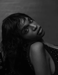 Black and white portrait of a model with textured short hair and glossy lips wearing an embellished knit top.