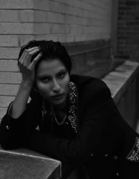 Model leaning against a brick wall wearing an embellished dark jacket with beaded lapels for Vogue Netherlands editorial.