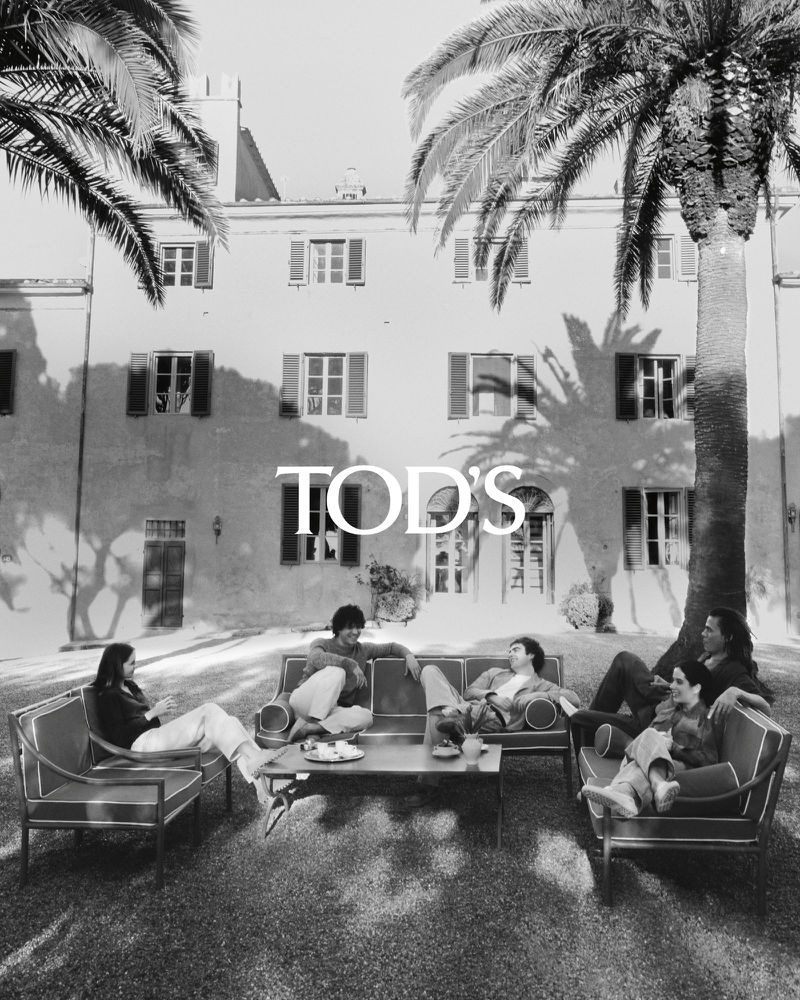 Black and white outdoor fashion shot: Six people are relaxing on outdoor furniture surrounded by palm trees and architecture.