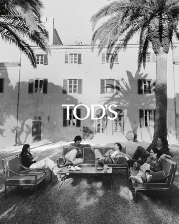 Black and white outdoor fashion shot: Six people are relaxing on outdoor furniture surrounded by palm trees and architecture.