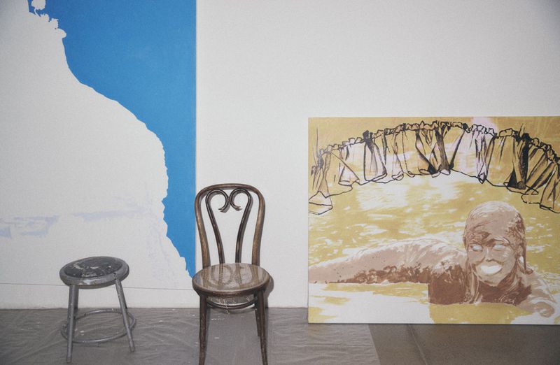 Interior shot featuring two chairs, an abstract painting of a figure in water, and a white and blue abstract design on a wall.
