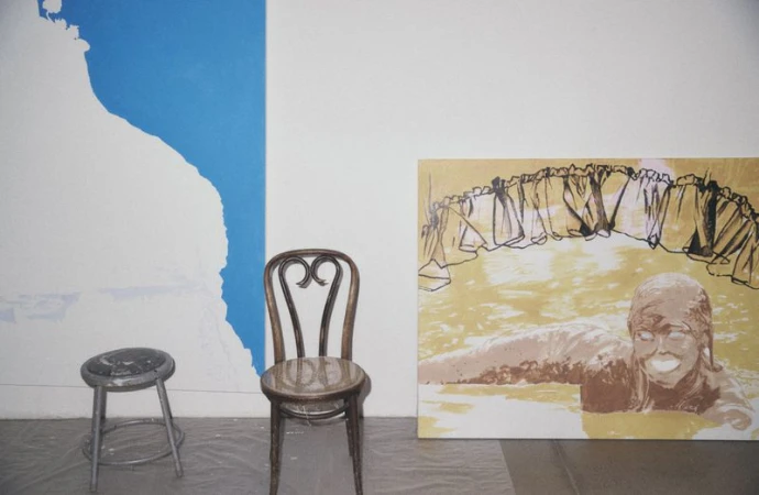 Interior shot featuring two chairs, an abstract painting of a figure in water, and a white and blue abstract design on a wall.