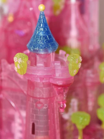 Close-up of a pink plastic toy castle turret with a blue cone roof and a yellow ball on top, featuring flowers.
