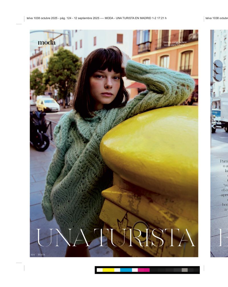 A young brunette model poses against a bright yellow bollard in a European city wearing a chunky knit sweater for a fashion editorial.