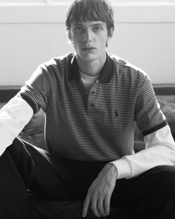 Black and white studio portrait of a young adult man wearing a striped polo shirt, looking at the camera with a neutral expression.
