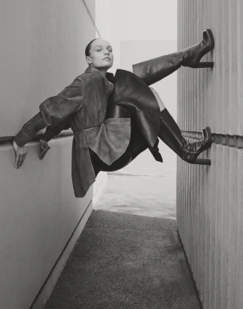 Monochrome fashion shot: a female model in a coat and high boots poses in an alleyway, emphasizing lines and geometric shapes.