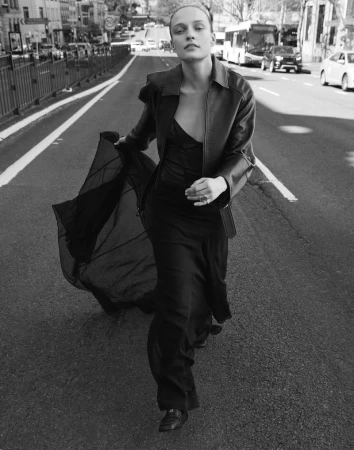 A fashionable woman in a black dress and jacket walks down a city street in a black and white fashion editorial.
