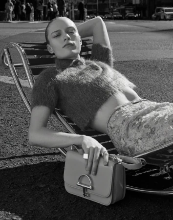 Monochrome outdoor fashion shot of a woman lying in a chair with a purse in her lap, with city street background, shallow depth of field.