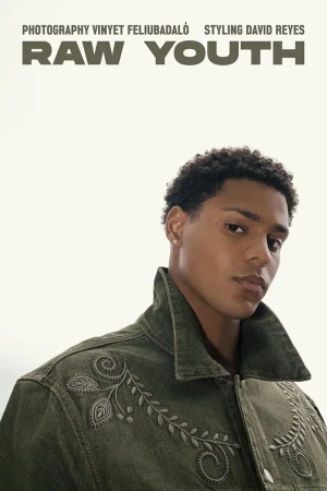 Portrait of a young adult male with curly hair wearing a green denim jacket, set against a neutral background in a fashion editorial.