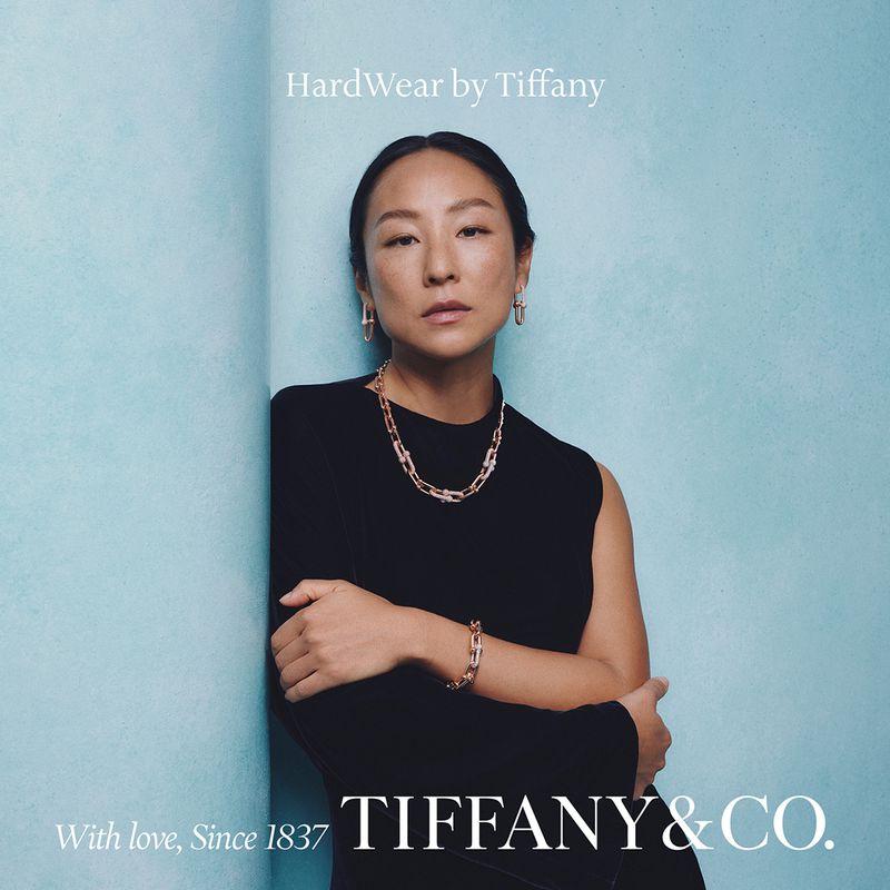 Elegant Asian woman showcases Tiffany & Co. HardWear jewelry against a textured blue backdrop, highlighting a necklace, earrings, and bracelet.