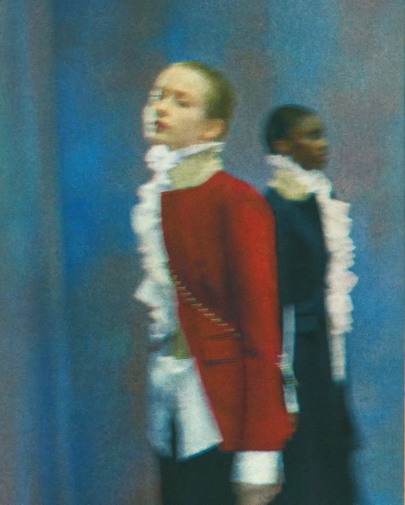 Two people standing in a blurry, painterly, soft-focus style. One person is in a red coat, the other in a black coat.