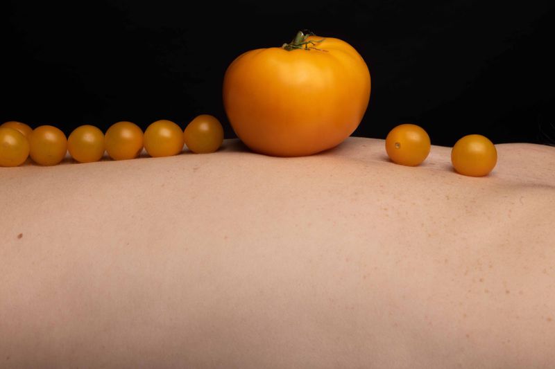 Still life featuring a variety of yellow tomatoes arranged on a pale surface against a dark background, creating a visually striking contrast.