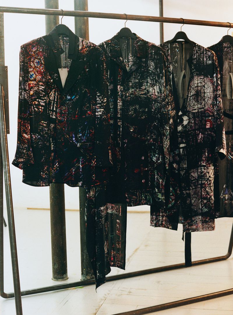 Abstract patterned coats and jackets on a metal rack, creating a fashion-forward display of outerwear in a bright indoor setting.